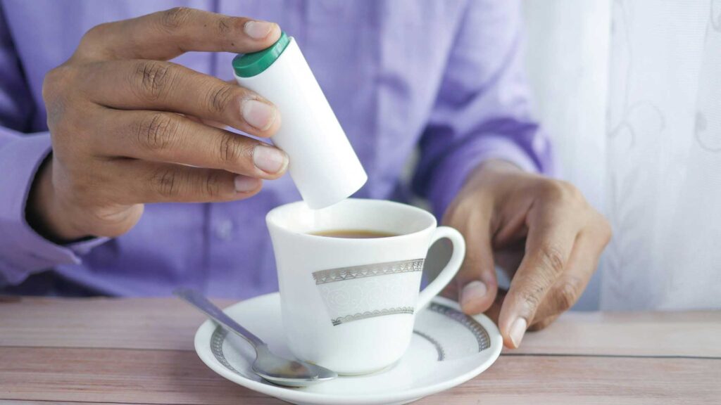 Mensch drückt Süßstoff aus einer Packung in eine Tasse Kaffee.