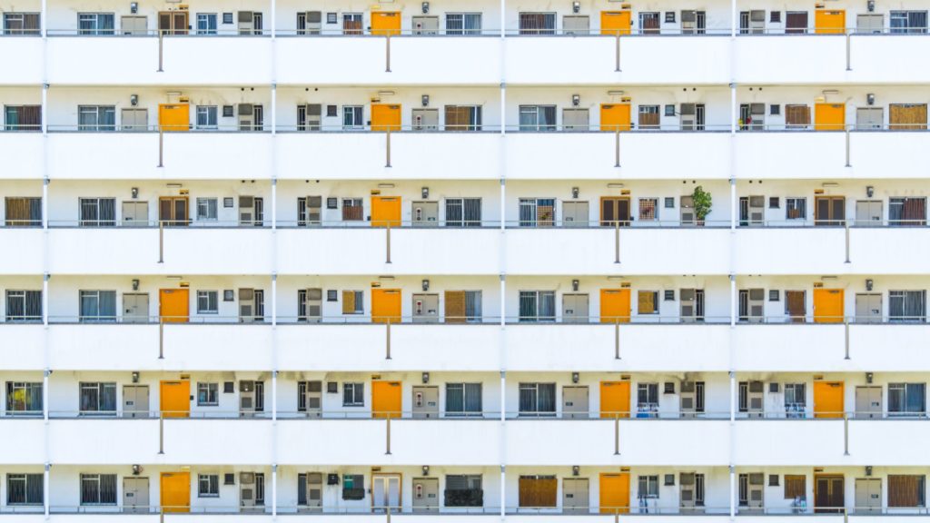 Weiße Wohnhausfassade mit Balkonen und regelmäßig angeordneten gelben Türen.