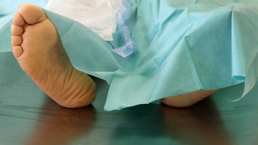 Ein Fuß guckt unter einem grünen Leichentuch der Pathologie hervor.