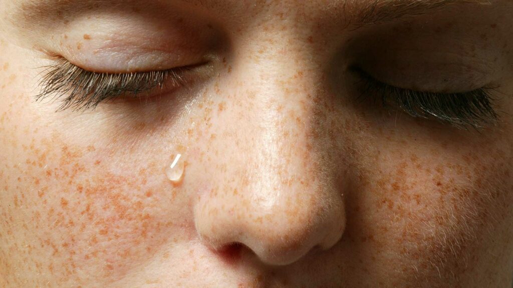 Nahaufnahme einer Augenpartie. Die Augen sind geschlossen, es läuft eine Träne die Wange runter.